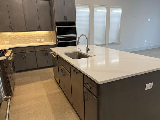 Kitchen with a sink, a center island with sink, stainless steel dishwasher, and dark brown cabinetry | Image 9