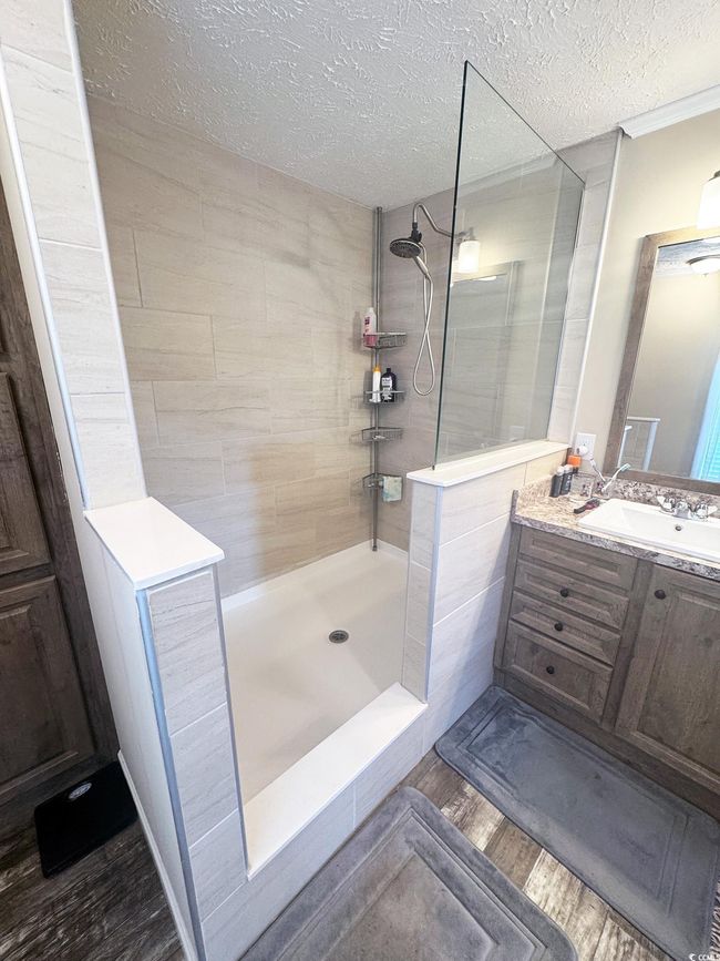 Full bath featuring a textured ceiling, a walk in shower, vanity, and wood finished floors | Image 23