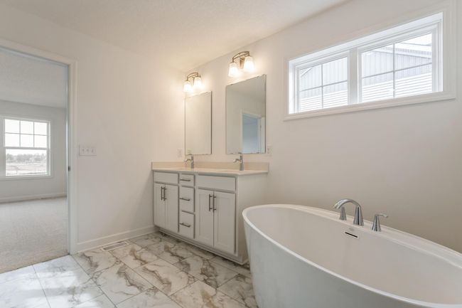 Photo is of the actual home. An extension of the primary suite, this private and spacious bath contains a double-vanity, a shower, a separate tub and a walk-in closet. | Image 8