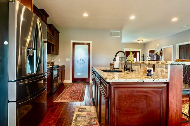 Kitchen with a sink, a kitchen island with sink, dark wood finished floors, stainless steel appliances, and visible vents | Image 10