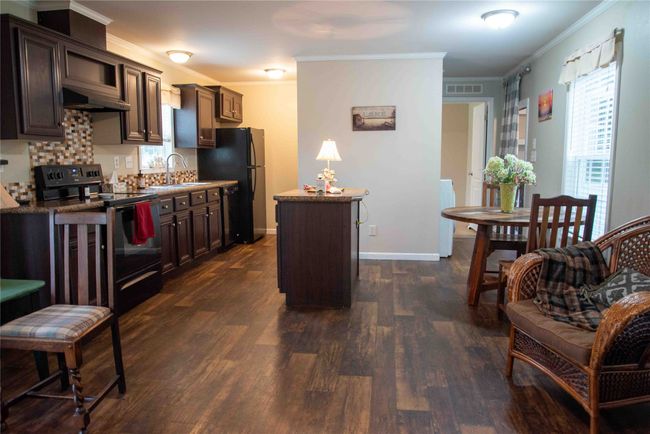 Kitchen with black appliances, under cabinet range hood, a sink, and dark wood-style floors | Image 23