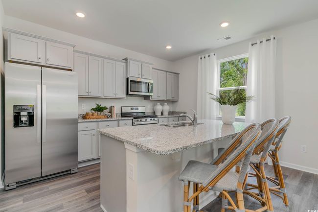 Kitchen with stainless steel appliances, a sink, wood finished floors, gray cabinets, and light stone countertops | Image 6