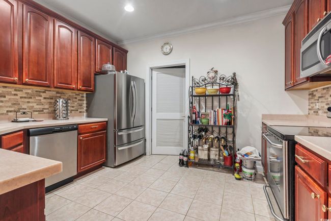Kitchen with stainless steel appliances, dark brown cabinets, crown molding, backsplash, and light countertops | Image 21