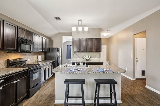Kitchen featuring black appliances, a breakfast bar, dark wood-type flooring, dark brown cabinetry, and lofted ceiling | Image 4