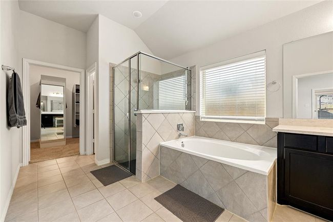 This primary bathroom is definitely move-in ready! Featuring a dark framed walk-in shower with tile surround, separate garden tub for soaking after a long day with custom tile detailing, dark stained cabinets with light countertops, spacious walk-in closet with shelving, high ceilings, custom paint, sleek and dark modern finishes. | Image 13