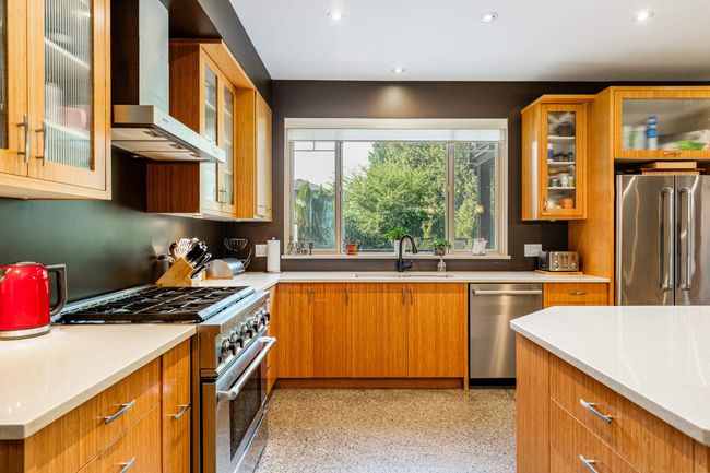 Kitchen with high quality appliances, wall chimney range hood, light countertops, recessed lighting, and glass insert cabinets | Image 9
