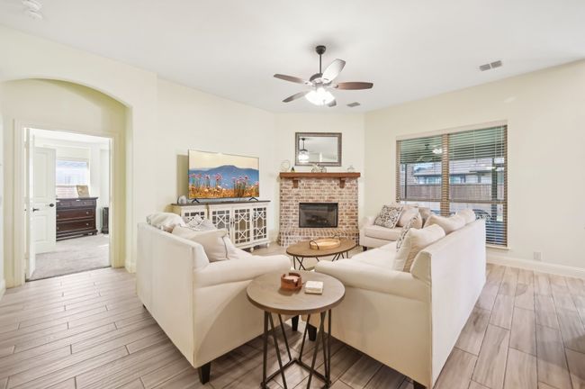 Living room with a brick fireplace, visible vents, wood tiled floor, and ceiling fan | Image 6