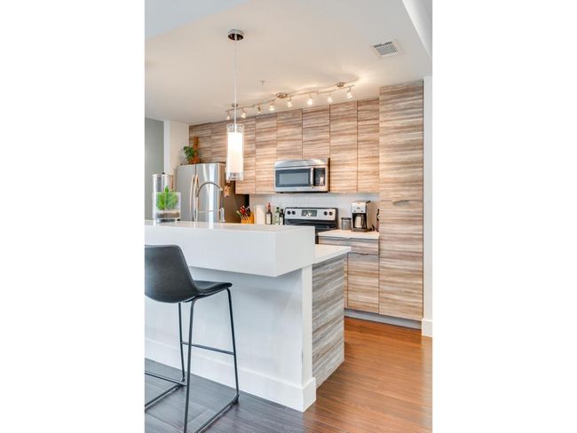 Kitchen featuring a breakfast bar, modern cabinets, appliances with stainless steel finishes, wood finished floors, and light countertops | Image 9