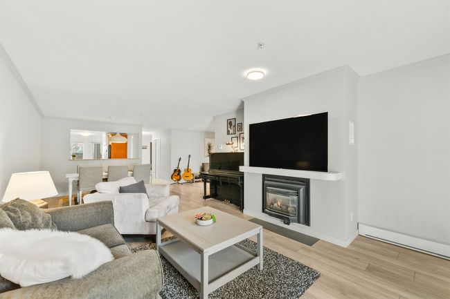 Living room with baseboard heating, light wood-style floors, a glass covered fireplace, ornamental molding, and baseboards | Image 12