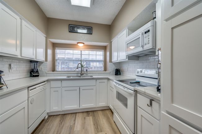 Kitchen with white cabinetry, sink, white appliances, a textured ceiling, and light hardwood / wood-style flooring | Image 4