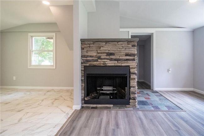 Unfurnished living room with a stone fireplace, tile patterned floors, and vaulted ceiling | Image 5