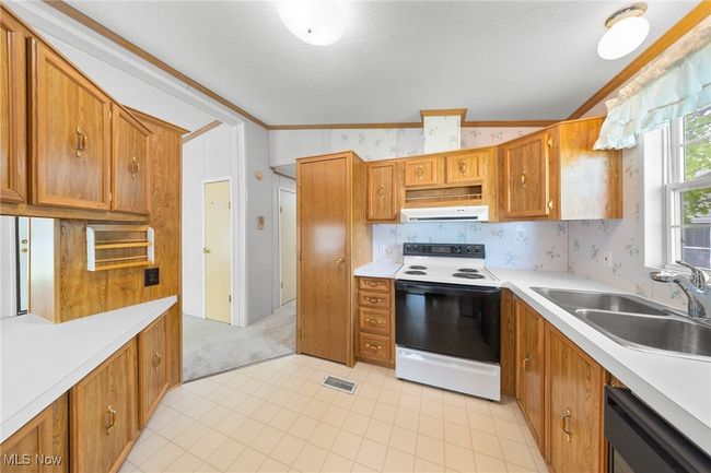 Kitchen featuring white electric range oven, a sink, extractor fan, light countertops, and wallpapered walls | Image 7