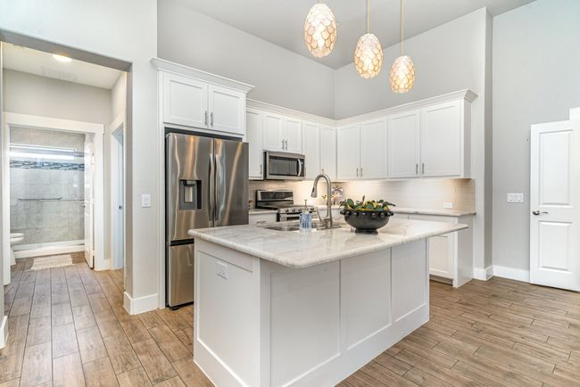 Kitchen featuring stainless steel appliances, white cabinetry, light wood finished floors, tasteful backsplash, and a high ceiling | Image 12