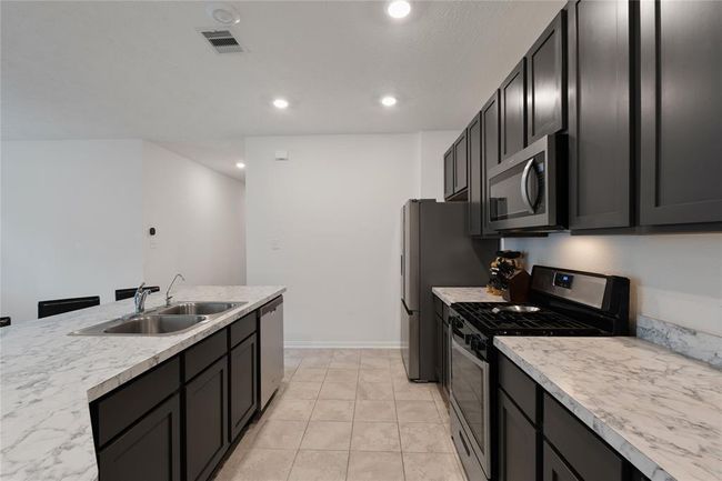 Modern kitchen with dark cabinetry, stainless steel appliances, and marble countertops. Features a dual sink and a spacious layout ideal for cooking and entertaining. | Image 5