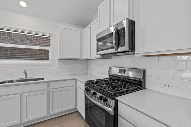 Kitchen with stainless steel appliances, light countertops, decorative backsplash, white cabinetry, and vaulted ceiling | Image 7