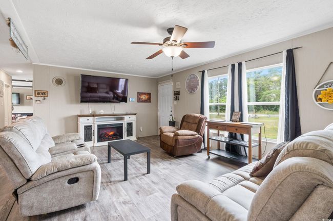 Living room featuring a textured ceiling, wood finished floors, ceiling fan, crown molding, and a warm lit fireplace | Image 9