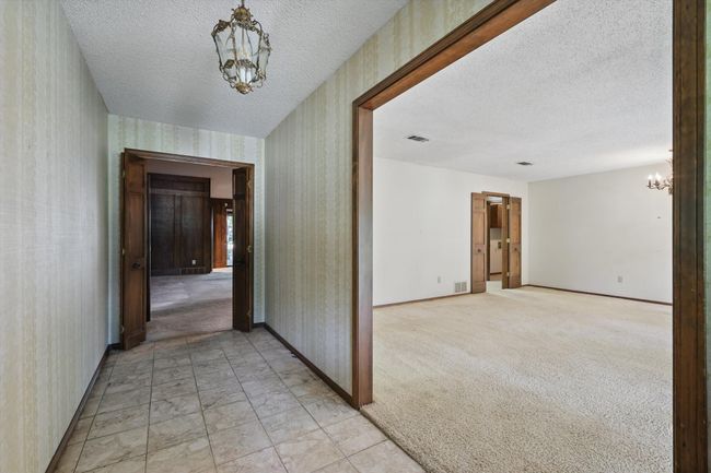Hall with a textured ceiling, wallpapered walls, a chandelier, baseboards, and visible vents | Image 6