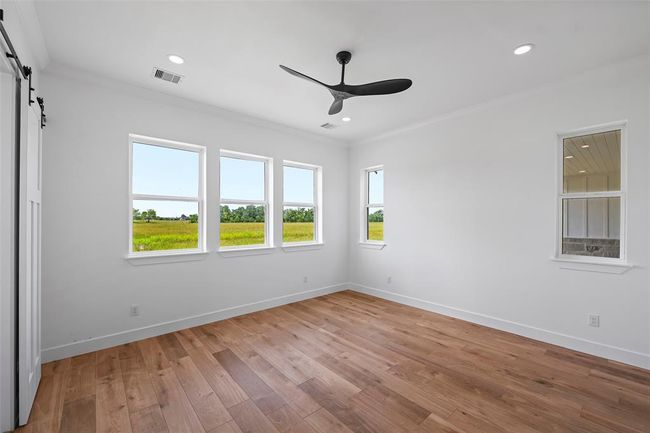 Spacious primary bedroom featuring elegant LVP floors, abundant natural light through multiple windows, and a sleek ceiling fan for comfort and style. | Image 23