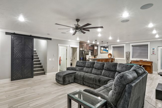 Living room with a barn door, crown molding, ceiling fan, light wood-style floors, and recessed lighting | Image 63