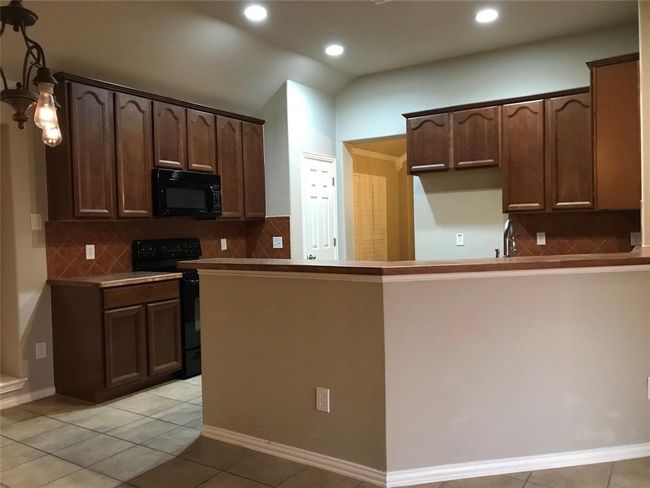 Kitchen with light tile patterned floors, black appliances, backsplash, and dark brown cabinets | Image 6
