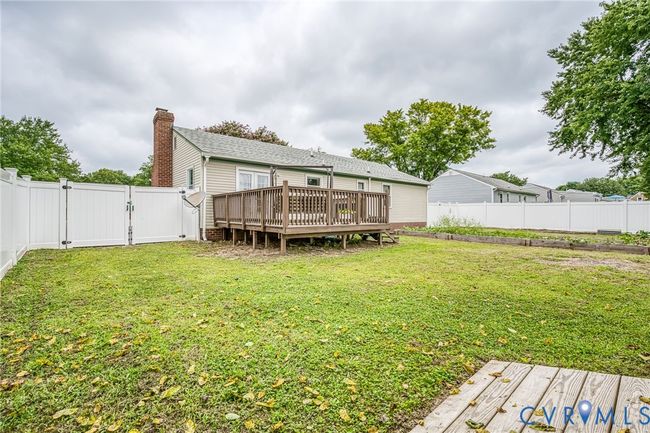 Rear view of house with a fenced backyard, a wooden deck, a gate, and a chimney | Image 21