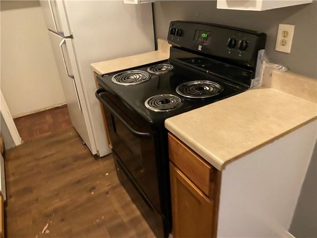 Kitchen with black range with electric stovetop, freestanding refrigerator, dark wood-style floors, brown cabinets, and light countertops | Image 5
