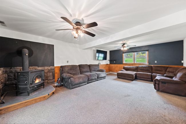 Living area with a wood stove, a ceiling fan, carpet flooring, and wainscoting | Image 23