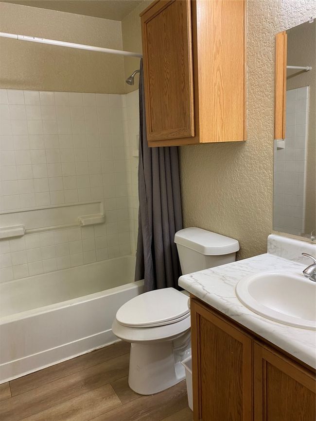 Bathroom with a textured wall, wood finished floors, vanity, shower / tub combo, and toilet | Image 7