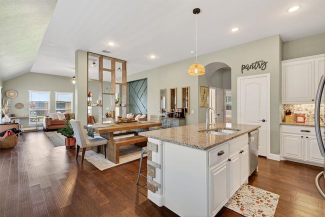 Kitchen with stainless steel dishwasher, open floor plan, dark wood-style floors, light stone countertops, and white cabinetry | Image 11