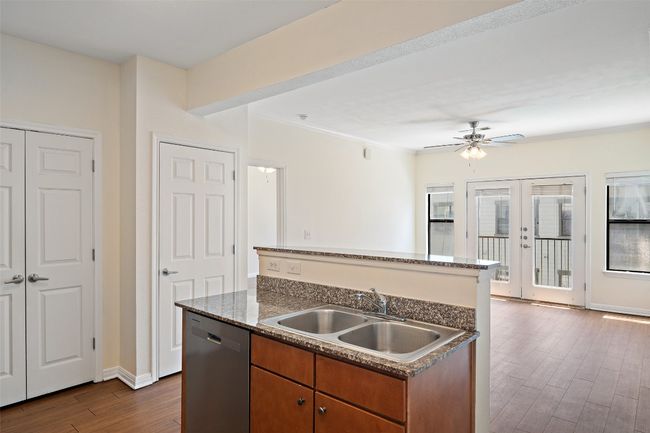 Kitchen featuring brown cabinetry, dark wood-style floors, dishwasher, a center island with sink, and ornamental molding | Image 5