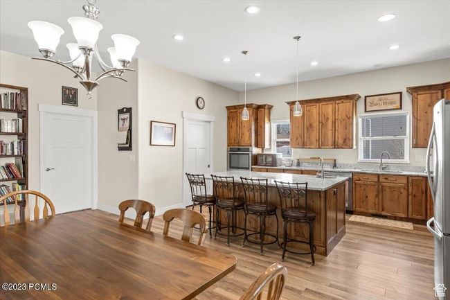 Kitchen with appliances with stainless steel finishes, brown cabinetry, an island with sink, light wood-style flooring, and a chandelier | Image 5