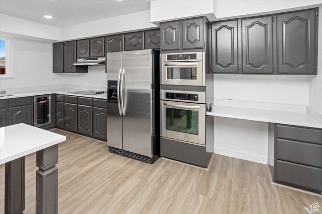 Kitchen with light countertops, light wood finished floors, wine cooler, appliances with stainless steel finishes, and under cabinet range hood | Image 11