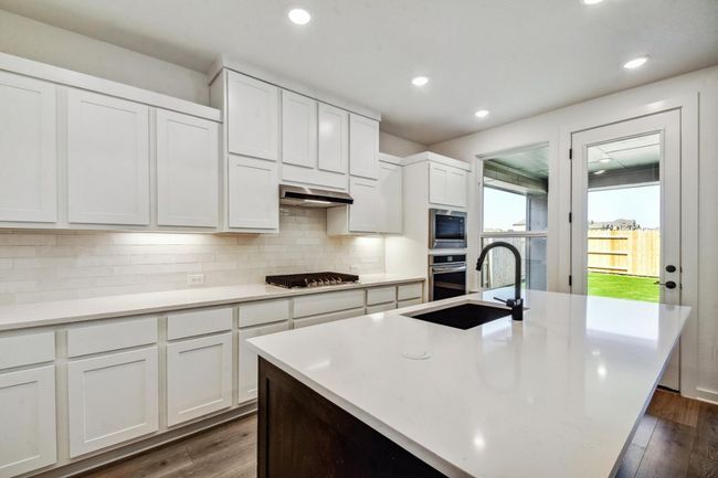 Kitchen featuring appliances with stainless steel finishes, exhaust hood, tasteful backsplash, light countertops, and white cabinets | Image 8