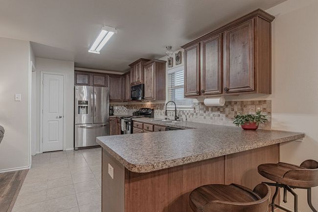 Kitchen with decorative backsplash, a peninsula, stainless steel appliances, a sink, and light tile patterned floors | Image 11