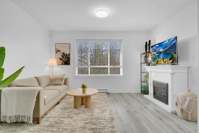 Living area featuring a glass covered fireplace, a baseboard heating unit, baseboards, and wood finished floors | Image 11