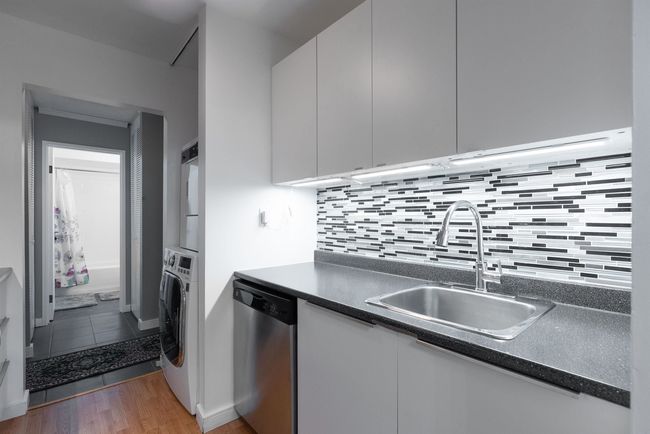 Kitchen with stacked washer and clothes dryer, stainless steel dishwasher, white cabinets, and a sink | Image 11