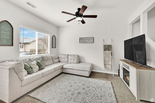 Carpeted living area with a glass covered fireplace, a ceiling fan, visible vents, and baseboards | Image 8