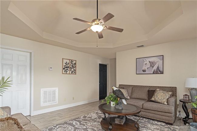 Living area featuring a tray ceiling, ceiling fan, light wood-type flooring, and baseboards | Image 6