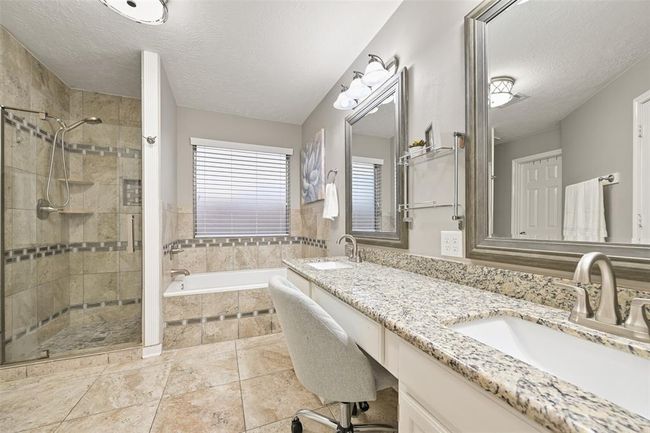 The elegant primary bath features granite-topped dual vanities, a built-in seated vanity, and a walk-in shower with decorative tile surround. A soaking tub and large-format tile floors complete this relaxing retreat. | Image 14