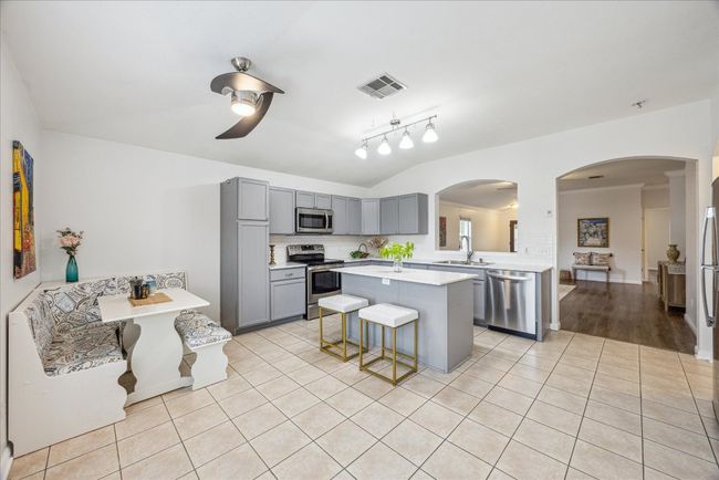 Kitchen with stainless steel appliances, gray cabinets, and light tile patterned floors, and large kitchen island, built-in breakfast area, track lighting and ceiling fan | Image 8