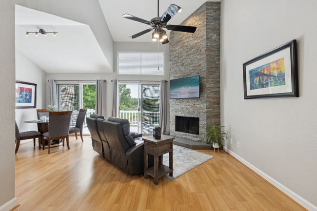 Living area with light wood finished floors, high vaulted ceiling, a fireplace, ceiling fan, and baseboards | Image 10