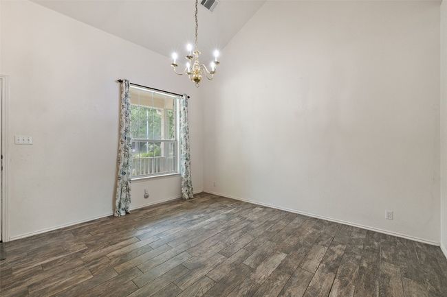 Empty room with an inviting chandelier, visible vents, baseboards, dark wood-type flooring, and vaulted ceiling | Image 8