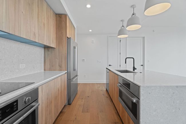 Kitchen featuring modern cabinets, appliances with stainless steel finishes, light stone counters, light wood-type flooring, and recessed lighting | Image 9