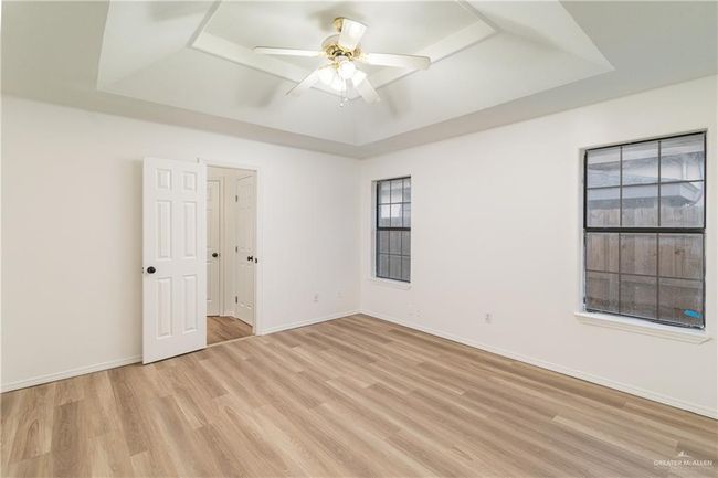 Empty room with light wood-style floors, a tray ceiling, baseboards, and a ceiling fan | Image 10