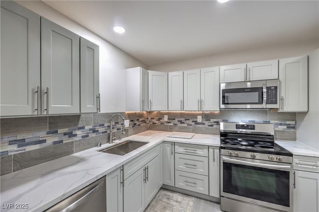 Kitchen featuring light stone countertops, backsplash, stainless steel appliances, and a sink | Image 13