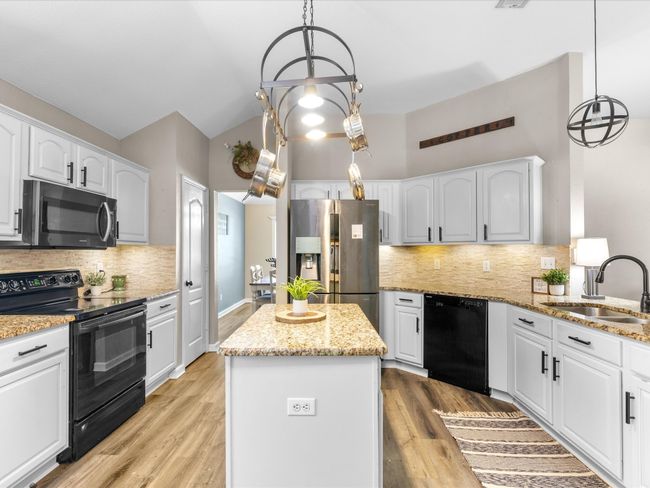 Kitchen featuring black appliances, a kitchen island, light stone countertops, decorative backsplash, and white cabinetry | Image 12