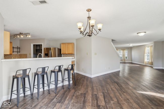 kitchen featuring stainless steel refrigerator with ice dispenser, light brown cabinets, a breakfast bar, backsplash, and dark wood-style flooring | Image 23
