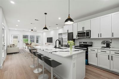 Kitchen with hanging light fixtures, sink, a kitchen island with sink, white cabinetry, and appliances with stainless steel finishes | Image 2