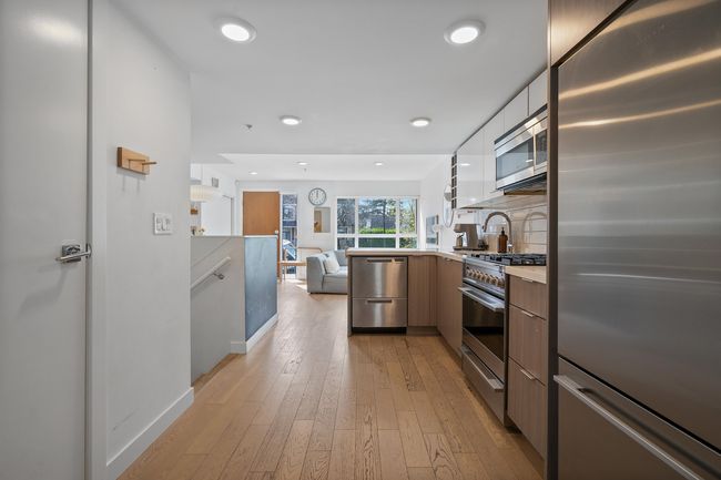 Kitchen featuring light wood-type flooring, light countertops, modern cabinets, decorative backsplash, and stainless steel appliances | Image 14