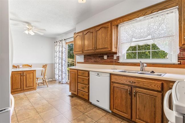 Kitchen featuring white appliances, a sink, brown cabinetry, a ceiling fan, and plenty of natural light | Image 36